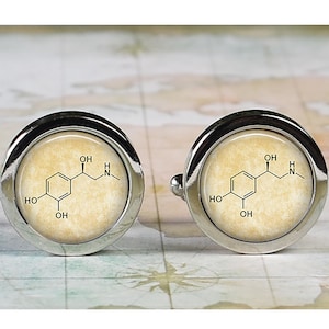 May include: A pair of silver cufflinks with a vintage-style background featuring a chemical formula for dopamine. The formula is printed in black on a cream-colored background.