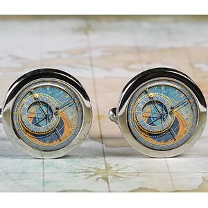 May include: A pair of silver cufflinks with a blue and gold clock face design. The clock face features Roman numerals and a detailed astronomical design.