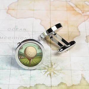 May include: Silver cufflinks with a round, white golf ball on a green field with a golf cart and a red flag. The cufflinks have a vintage design with the text "Country Club" and "Sept 24" on the image.