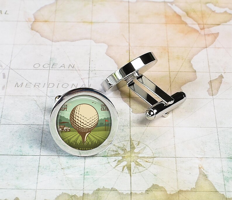 May include: Silver cufflinks with a round, white golf ball on a green field with a golf cart and a red flag. The cufflinks have a vintage design with the text "Country Club" and "Sept 24" on the image.