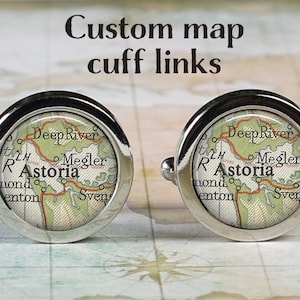 May include: Pair of silver cuff links with a map design. The map features the name "Astoria" in a vintage style, with the text "Custom map cuff links" above the cuff links. The cuff links are round with a shiny silver finish.