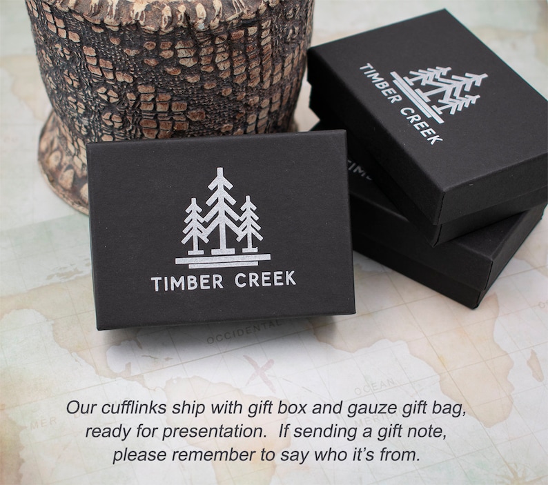 Puede incluir: Caja de regalo negra con un logotipo blanco de tres &aacute;rboles estilizados y el texto "TIMBER CREEK".