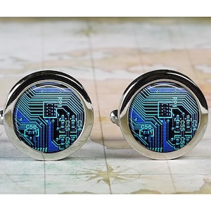 May include: A pair of silver cufflinks with a blue and green circuit board design. The cufflinks are round and have a silver border.