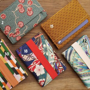 May include: A collection of nine different fabric card holders with elastic bands. The card holders feature various patterns, including floral, geometric, and abstract designs. The numbers 2, 15, 18, 22, and 30 are visible on the card holders.