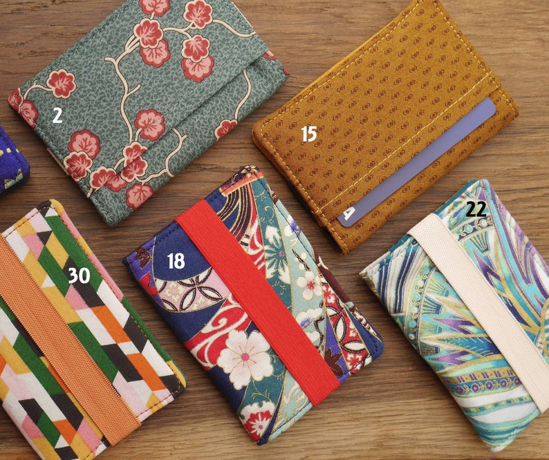 May include: A collection of nine different fabric card holders with elastic bands. The card holders feature various patterns, including floral, geometric, and abstract designs. The numbers 2, 15, 18, 22, and 30 are visible on the card holders.