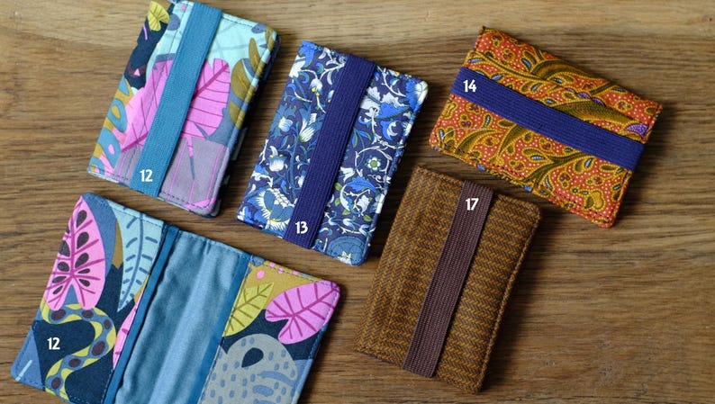 May include: Six different fabric card holders with elastic bands. The card holders are in various patterns and colors, including blue, brown, orange, and pink.