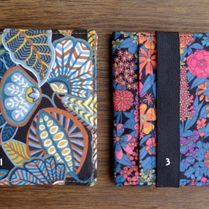 May include: Two fabric card holders with floral patterns. The holder on the left has a blue, green, and brown floral pattern. The holder on the right has a pink, orange, and blue floral pattern with a black elastic band.