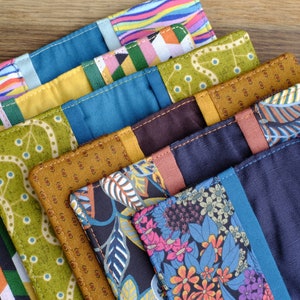 May include: A stack of eight colorful fabric pouches with different patterns, including stripes, geometric shapes, and floral designs. The pouches are made of a variety of fabrics, including cotton and linen. They are all sewn with a contrasting thread.