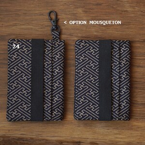 May include: Two black and gold patterned fabric card holders with a black elastic band. The card holder on the left has a black metal clip attached. The text "24" is printed on the front of the card holder.