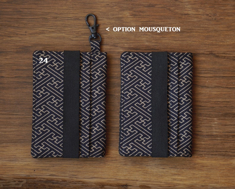May include: Two black and gold patterned fabric card holders with a black elastic band. The card holder on the left has a black metal clip attached. The text "24" is printed on the front of the card holder.