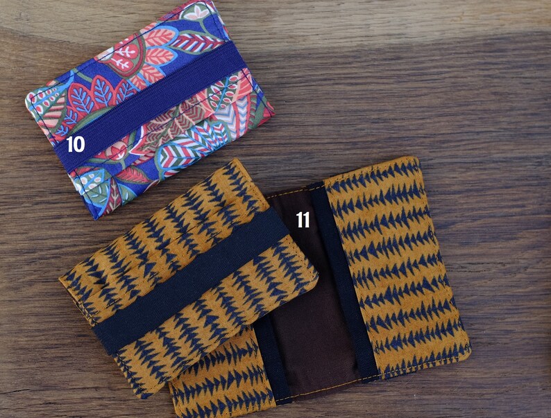 May include: Two fabric card holders with elastic closures. The first holder has a blue background with a colorful floral pattern and the text "10". The second holder has a brown background with a black geometric pattern and the text "11".