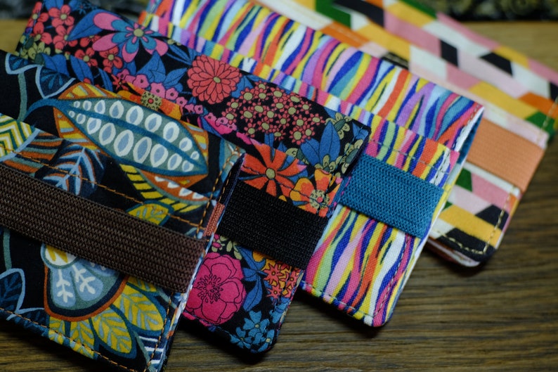 May include: Four colorful fabric wallets with different patterns. Each wallet has a brown, black, or blue strap.
