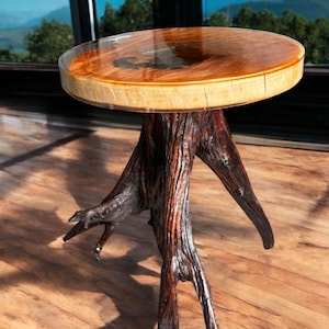 May include: A unique side table with a round wooden top and a clear resin finish. The base is crafted from natural tree roots, showcasing a dark brown, textured appearance. The table is a blend of natural and modern design.