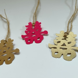 Puede incluir: Tres recortes de papel del carácter chino para "doble felicidad" en cuerdas de hilo. Un recorte es dorado, uno es rosa y uno es marrón.