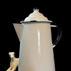 Peut inclure: Cafetière en émail blanc avec une poignée et un couvercle noirs. La cafetière a un aspect vintage avec quelques éclats de peinture noire.