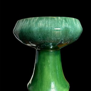 May include: A green ceramic vase with a wide, shallow bowl and a tall, slender base. The vase has a mottled glaze with a light green and white pattern.