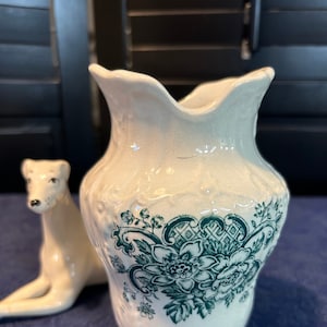 Peut inclure: Un pichet en céramique blanche avec un motif floral vert. Le pichet a une large ouverture et une anse.