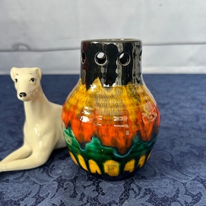 Peut inclure: Un petit vase en céramique coloré avec un bord noir et des trous. Le vase a un glaçage jaune, orange, vert et noir.