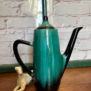 May include: A tall, green and black ceramic teapot with a spout and a handle. The teapot has a glazed finish with a streaky pattern.