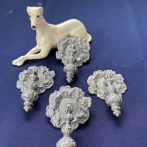 May include: Four ornate silver-toned cabinet door pulls with a decorative floral design. Each pull has a round base and a decorative knob.
