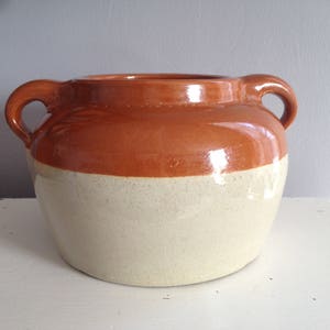 Può includere: Un'anfora in ceramica smaltata marrone e bianca con due manici.