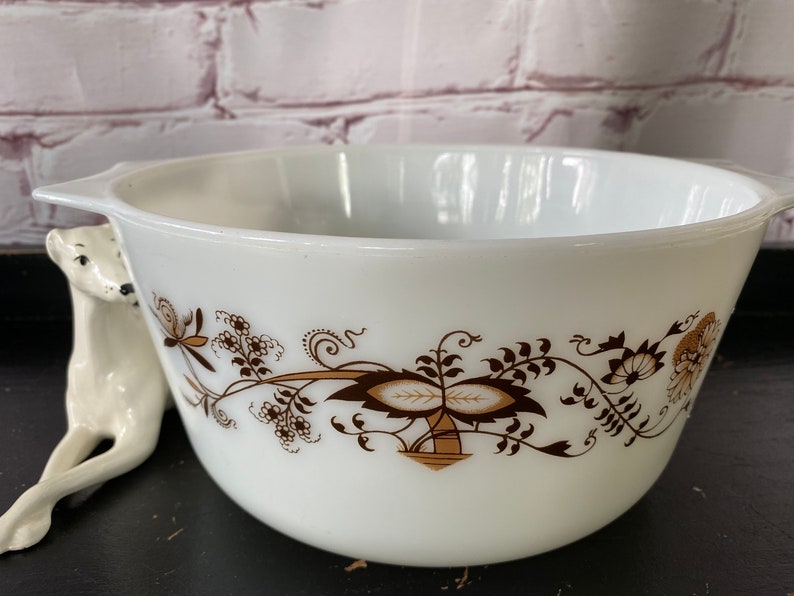 May include: White mixing bowl with a brown floral design. The bowl has a handle on one side.