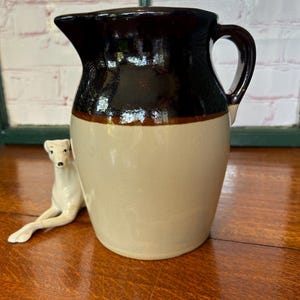May include: A brown and white glazed ceramic jug with a handle. The jug has a brown top and a white bottom.