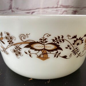 May include: White ceramic mixing bowl with a brown and white floral design. The bowl has a rounded shape and a wide rim.
