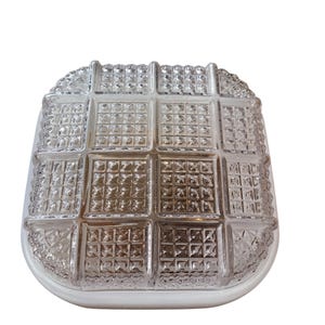 Peut inclure: Un luminaire de plafond en verre transparent de forme carrée avec un motif en grille. Le verre est texturé avec de petits carrés.