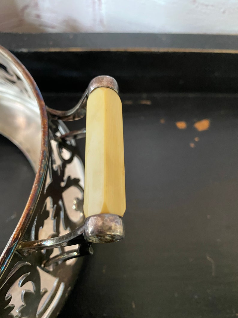 K&ouml;nnte beinhalten: Eine silberne Servierplatte mit einem verzierten Design und einem cremefarbenen Griff.