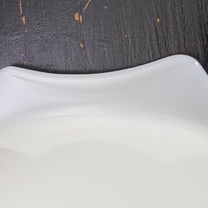 May include: White glass pie plate with a slightly wavy edge. The plate is made of opaque white glass and has a smooth surface.