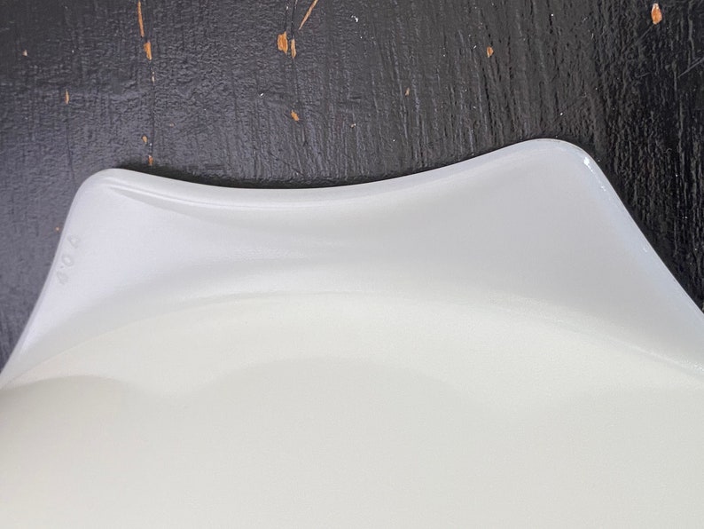 May include: White glass pie plate with a slightly wavy edge. The plate is made of opaque white glass and has a smooth surface.