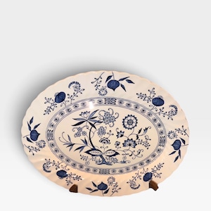 May include: An oval ceramic platter with a scalloped edge, featuring a white base decorated with a blue floral pattern. The design includes intricate botanical motifs, stylised flowers, and small fruit-like elements arranged in a central cluster.