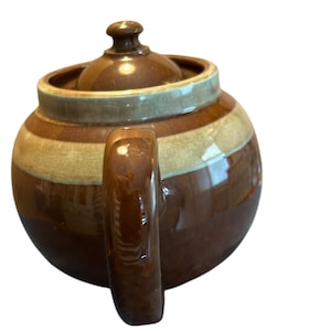 May include: A brown ceramic teapot with a lid and handle. The teapot has horizontal stripes in shades of brown and tan. The handle is a solid brown color, and the lid has a small knob.