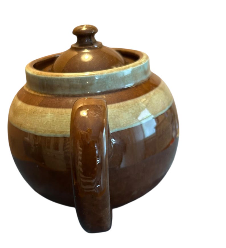 May include: A brown ceramic teapot with a lid and handle. The teapot has horizontal stripes in shades of brown and tan. The handle is a solid brown color, and the lid has a small knob.