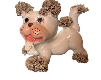 May include: A ceramic figurine of a dog with brown fur, a pink tongue sticking out, and brown eyes. The dog is in a running pose.