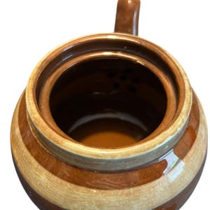 May include: A brown and beige striped ceramic teapot, viewed from above. The teapot has a handle and a spout. The interior is a darker brown. The ceramic has a crackled glaze.