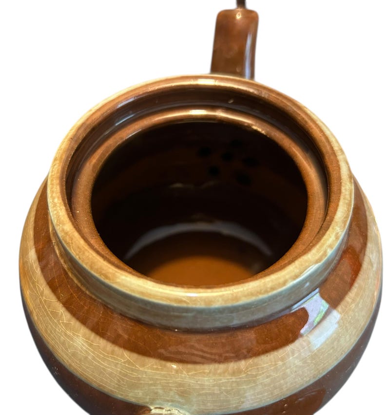May include: A brown and beige striped ceramic teapot, viewed from above. The teapot has a handle and a spout. The interior is a darker brown. The ceramic has a crackled glaze.