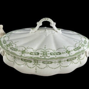 Może przedstawiać: Biała porcelanowa miska do serwowania z zielonym wzorem kwiatowym i pokrywką z ozdobnym uchwytem.