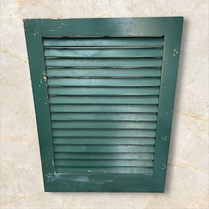 Peut inclure: Un volet en bois vert foncé avec des lamelles horizontales. Le volet est de forme rectangulaire avec un sommet légèrement incliné. La peinture montre des signes d'usure, lui donnant un aspect vintage. Dimensions: environ 60 cm x 80 cm.