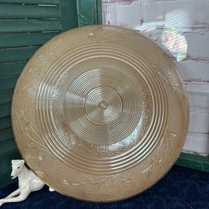 May include: A large, round, brown glass plate with a concentric circle design and a floral pattern around the edge.