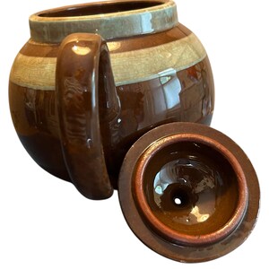 May include: A brown ceramic teapot with a matching lid. The teapot has a rounded body with a handle and a spout. The lid is round with a small hole in the center. The teapot has a striped design in shades of brown and tan.