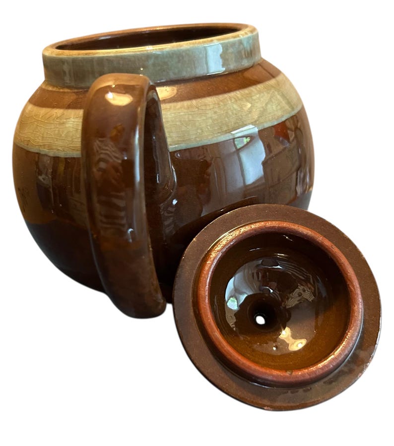 May include: A brown ceramic teapot with a matching lid. The teapot has a rounded body with a handle and a spout. The lid is round with a small hole in the center. The teapot has a striped design in shades of brown and tan.