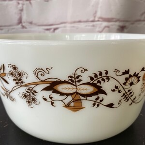May include: White ceramic mixing bowl with a brown floral design. The design features stylized leaves, flowers, and a central motif of two overlapping leaves.