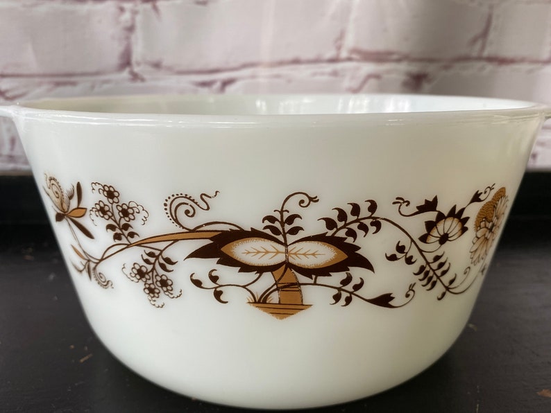 May include: White ceramic mixing bowl with a brown floral design. The design features stylized leaves, flowers, and a central motif of two overlapping leaves.