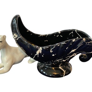 May include: A black and white ceramic planter shaped like a crescent moon with a white glazed finish. The planter has a glossy finish and a white base.
