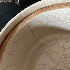 K&ouml;nnte beinhalten: Eine wei&szlig;e Keramiksch&uuml;ssel mit braunem Rand und einer craquel&eacute;-Glasur. Die Sch&uuml;ssel hat ein Netz feiner Risse &uuml;ber die gesamte Oberfl&auml;che.