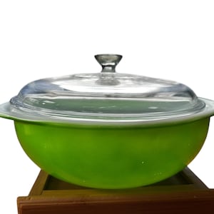 May include: A green glass baking dish with a clear glass lid. The dish is sitting on a wooden surface.