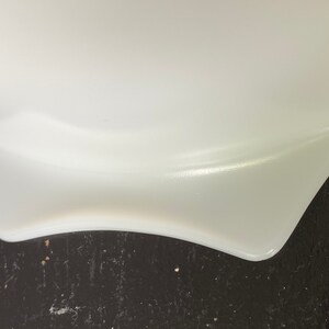 May include: Close-up of the bottom edge of a white, ceramic bowl. The bowl has a slightly wavy edge and is resting on a dark surface.