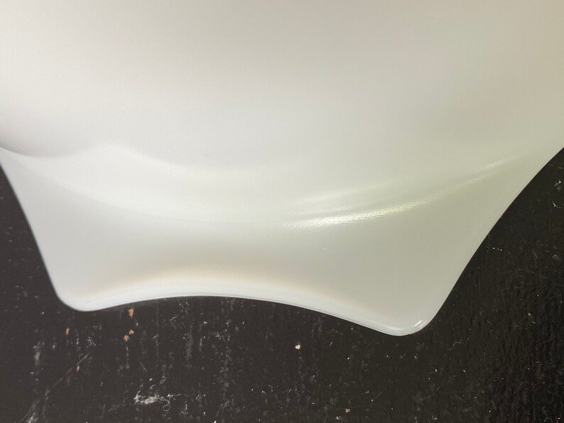 May include: Close-up of the bottom edge of a white, ceramic bowl. The bowl has a slightly wavy edge and is resting on a dark surface.